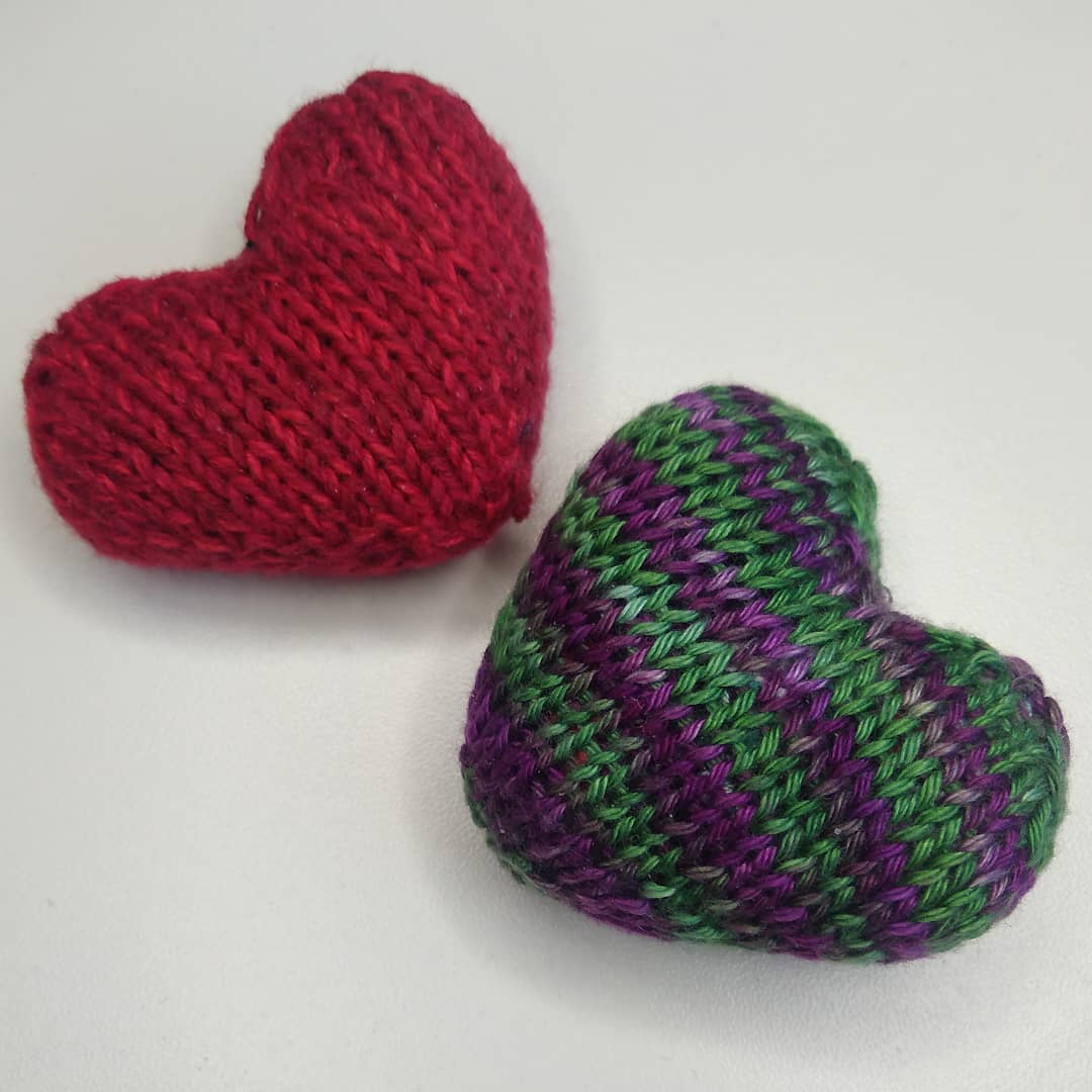 Two handknit hearts, one in red, one in purple and green stripes