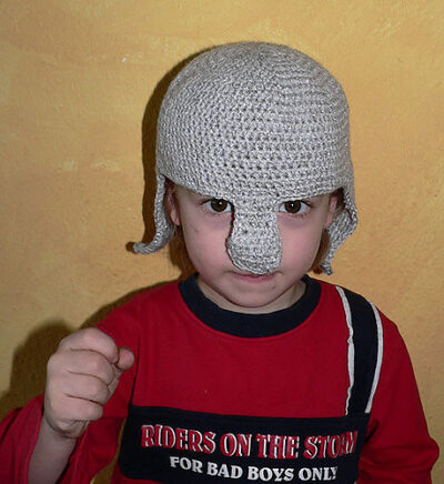 Child wearing a red sweater and a crochet knight's helmet, holding their hand up as if they held a sword