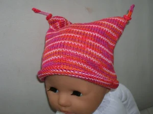 A baby doll wears a pink striped hat with a rolled brim and tied i-cords at the two points at the top