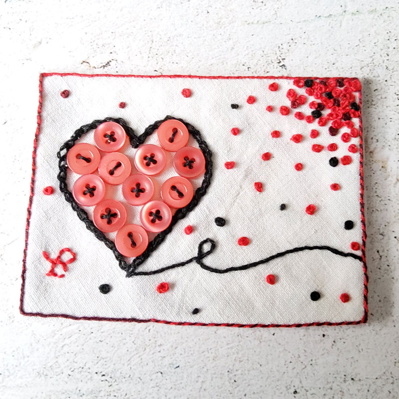 ATC with a heart of red buttons, outlined by black embroidery. The background is irregularly filled with French knots in red and black