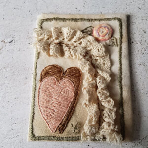 ATC on coffee stained fabric in pale pink, green and brown, with a bit of cream coloured lace. Bottom left has a pink heart with a brown one behind, frame is done in green. Top right corner has a multi-coloured pink rose