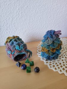 Two crochet dragon-scale dice bags in multi-coloured yarn sit on a table.